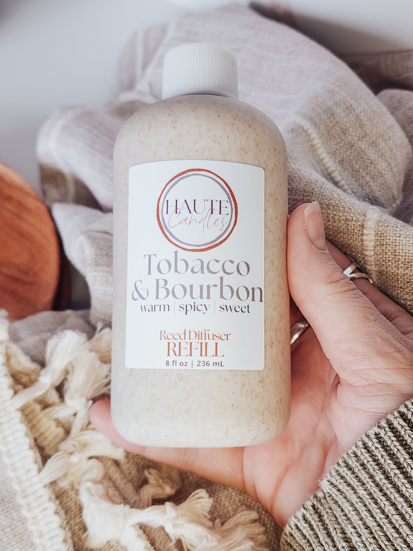 Hand holding a bottle of 'Tobacco & Bourbon' room diffuser refill with a soft, neutral background.